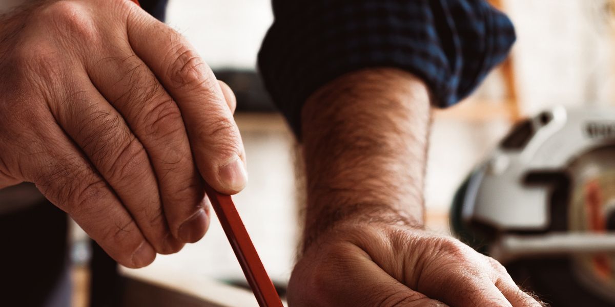 carpenter makes pencil marks on a wood plank